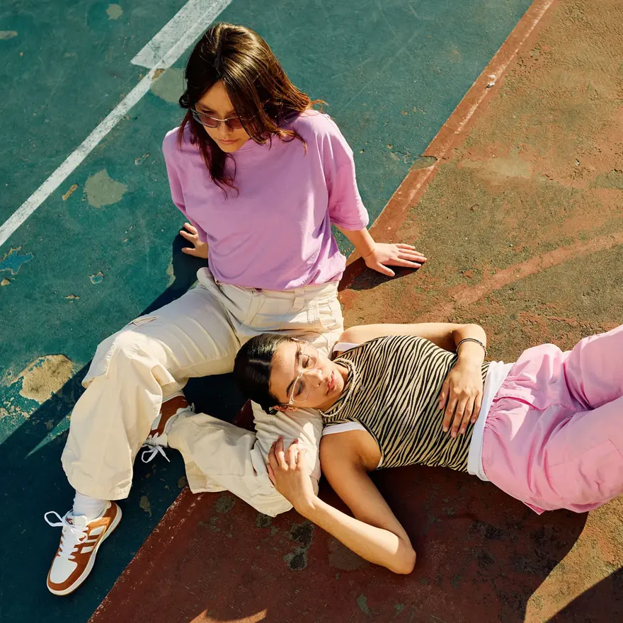 Bilde i fugleperspektiv på to damer i lyse og rosa klær som sitter på bakken