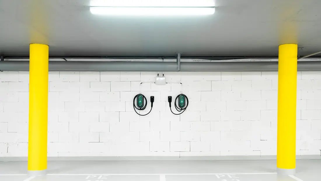 To ladekabler til el-bil henger på hvit vegg i garasje med to gule søyler på hver side