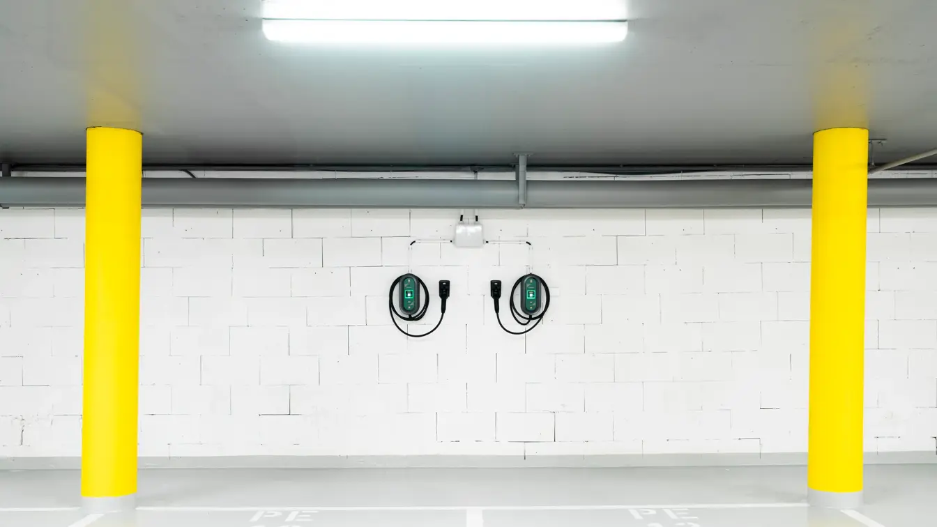 To ladekabler til el-bil henger på hvit vegg i garasje med to gule søyler på hver side