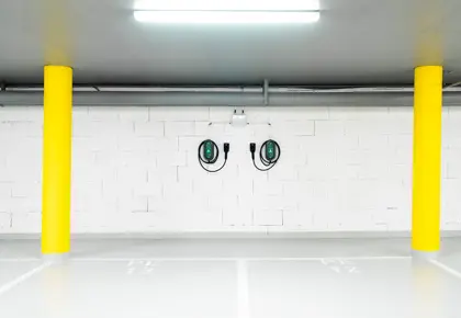 To ladekabler til el-bil henger på hvit vegg i garasje med to gule søyler på hver side