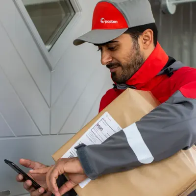 Mann iført arbeidsklær fra Posten står utenfor en dør med en pakke under armen som skal leveres