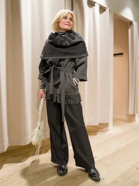 Dame i grå jakke med belte, sjal, hvit veske, grå bukse og sorte sko