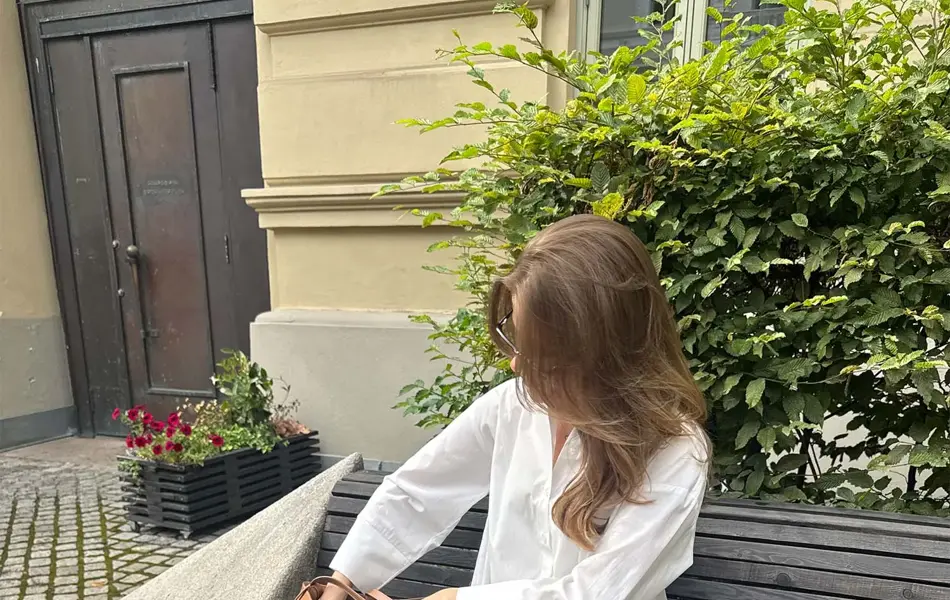 dame sitter på en benk med hvit skjorte, gråbeige bukse, hvite hæler