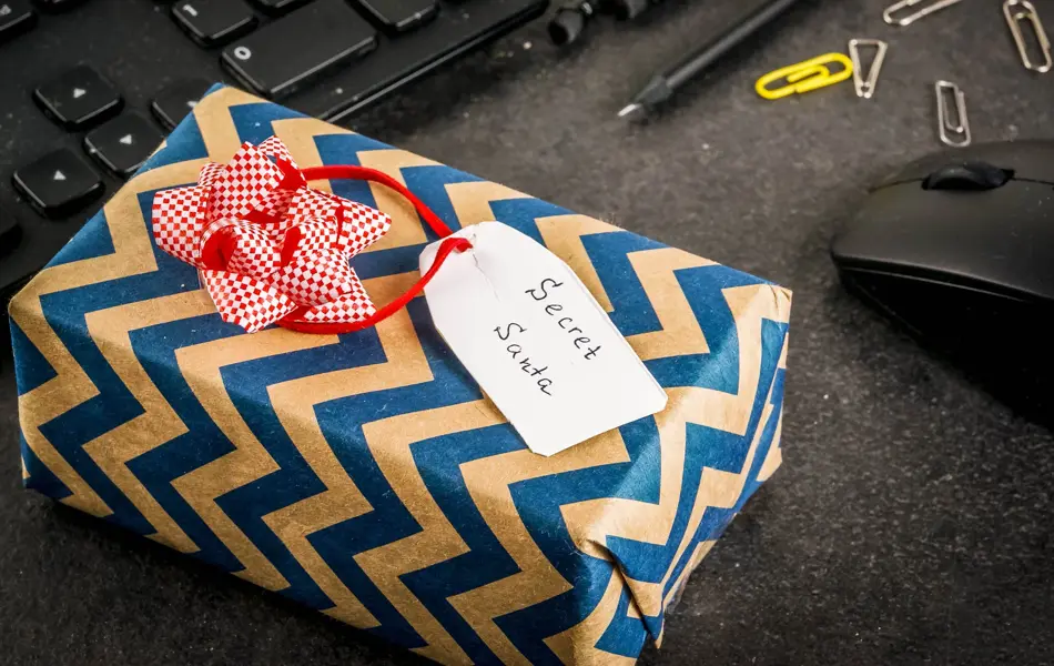 Office Christmas celebration concept, the idea of sharing gifts secret Santa. Keyboard, mouse, notebook, pens, pencils, Christmas gift. Black office table, copy space