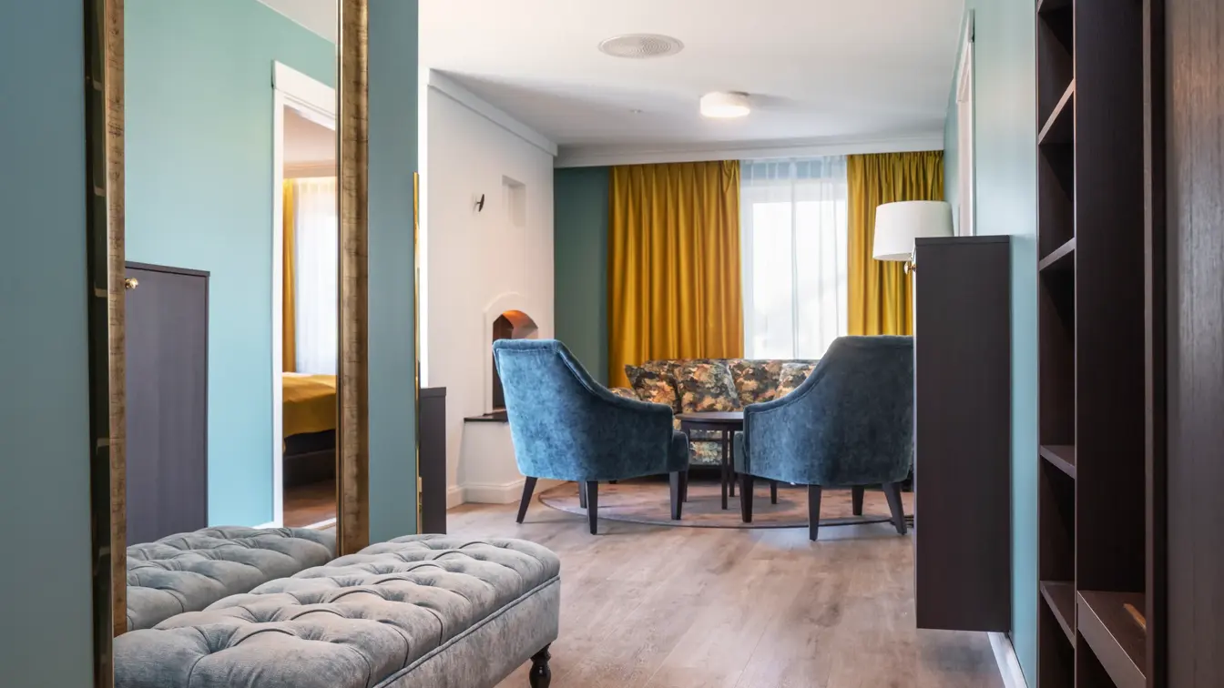 Peis, sofa, gule gardiner,  2 blå lenestoler, salongbord, parkettgulv, vindu, veggspeil, blå puff