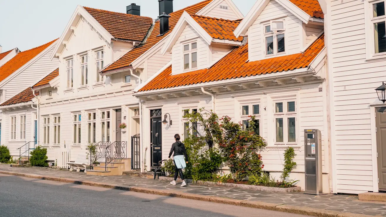 Posebyen i Kristiansand, med hvite, gamle trehus. En kvinne går på fortauet foran husene.