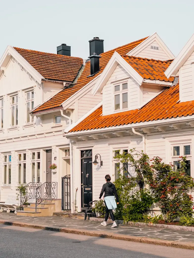 Posebyen i Kristiansand, med hvite, gamle trehus. En kvinne går på fortauet foran husene.