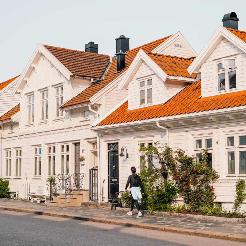 Posebyen i Kristiansand, med hvite, gamle trehus. En kvinne går på fortauet foran husene.