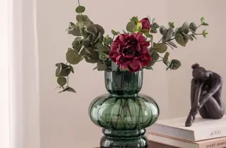 En grønn vase med røde og grønne blomster.