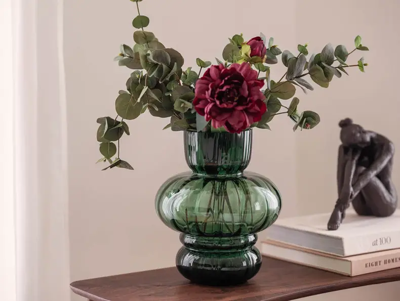En grønn vase med røde og grønne blomster.