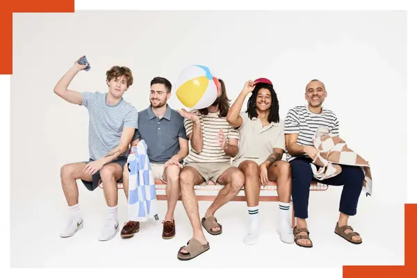 En gjeng menn sitter på en benk med håndkle, badeball, shorts og t-skjorte og skjorter.