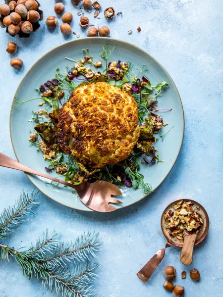 Blå tallerken med et helt stekt blomkålhode, med hasselnøtter ved siden