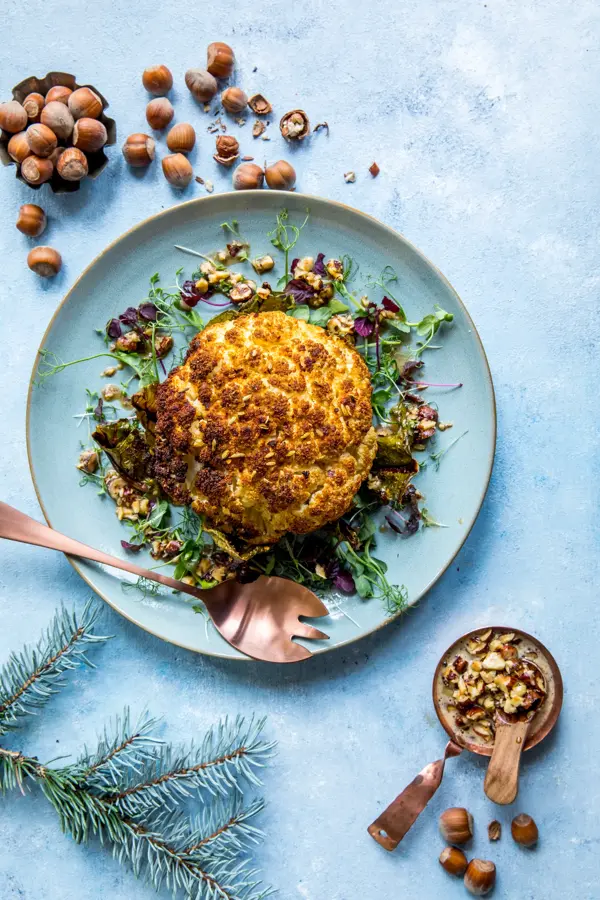 Blå tallerken med et helt stekt blomkålhode, med hasselnøtter ved siden