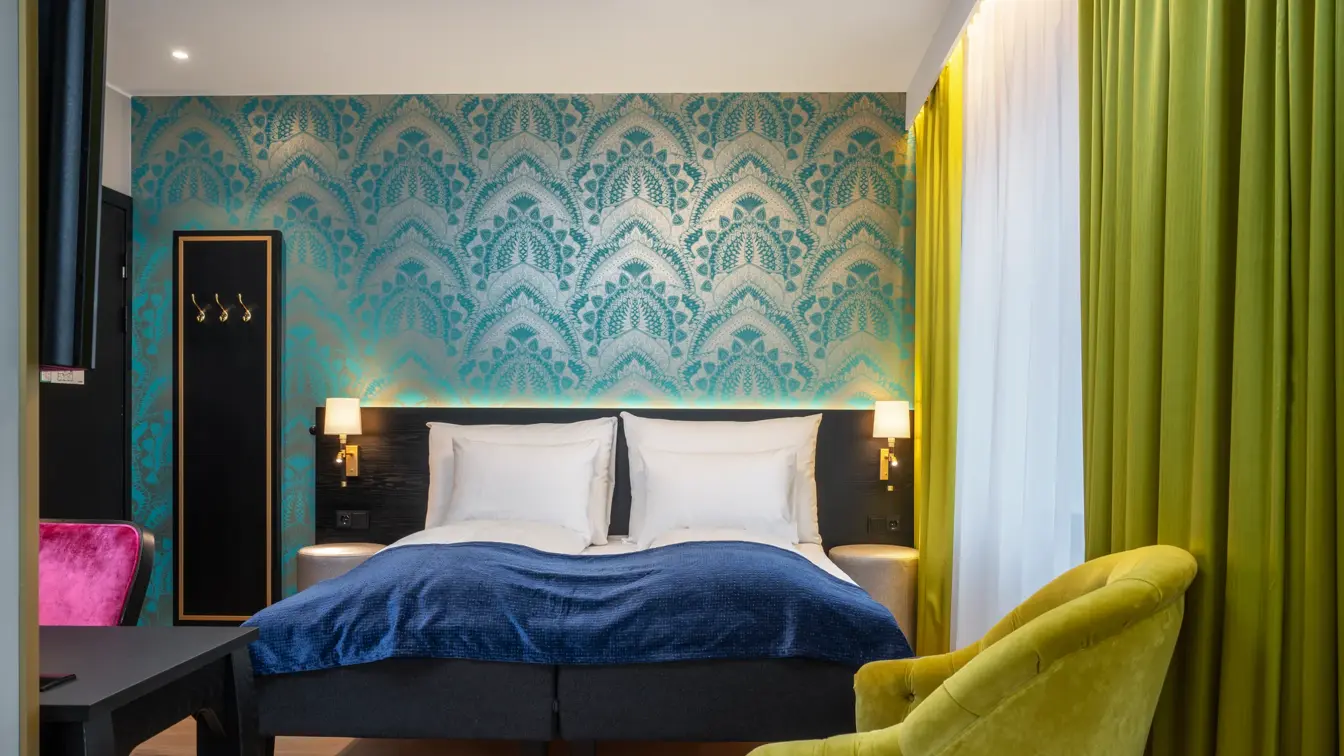 Blå tapetvegg, vindu, gul lenestol, dobbeltseng, skrivebord, rosa stol