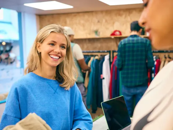 Woman Buying Shirt From Female Sales Assistant At Cash Desk In Fashion Store