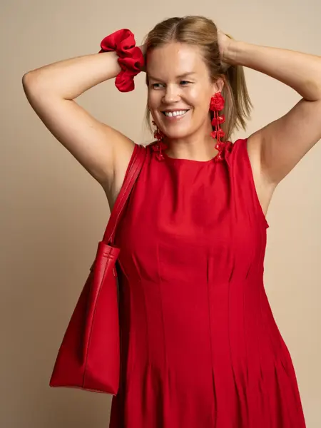 Damemodell med rød schrunchie på armen, lange rød øredobber, rød veske over skulderen og rød kjole.