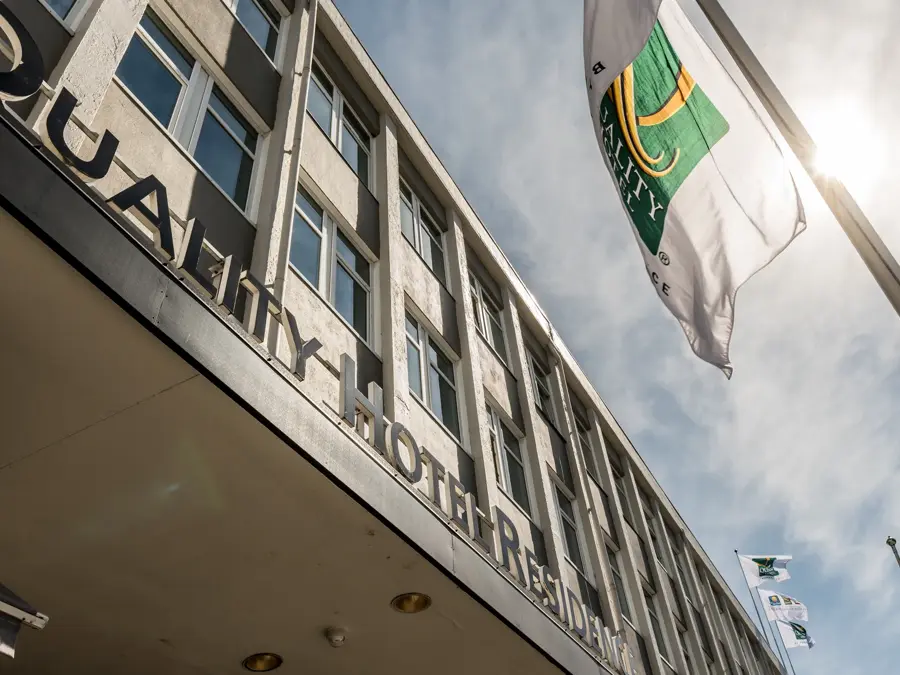 Fasaden til Quality Hotel Residence med flagg og blå himmel