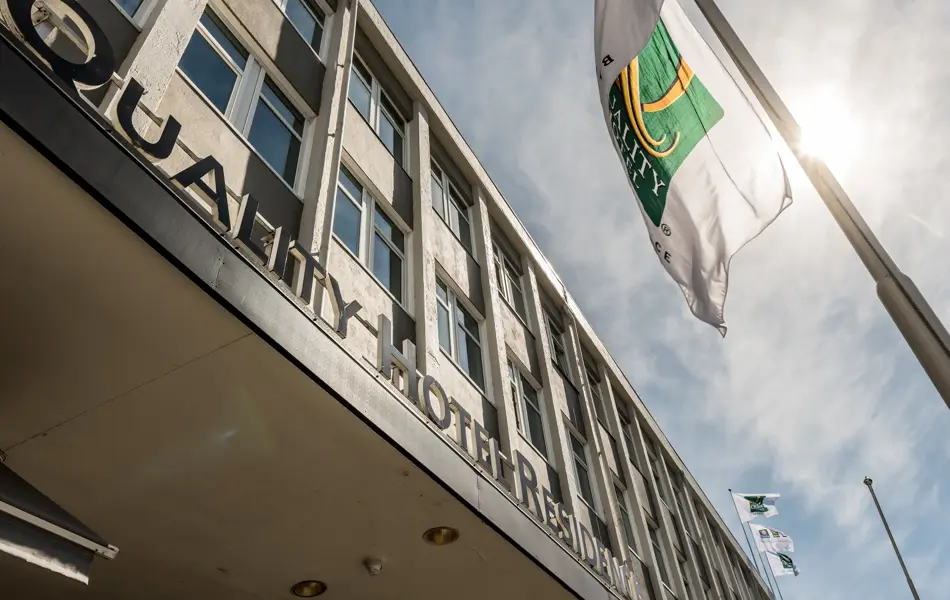 Fasaden til Quality Hotel Residence med flagg og blå himmel