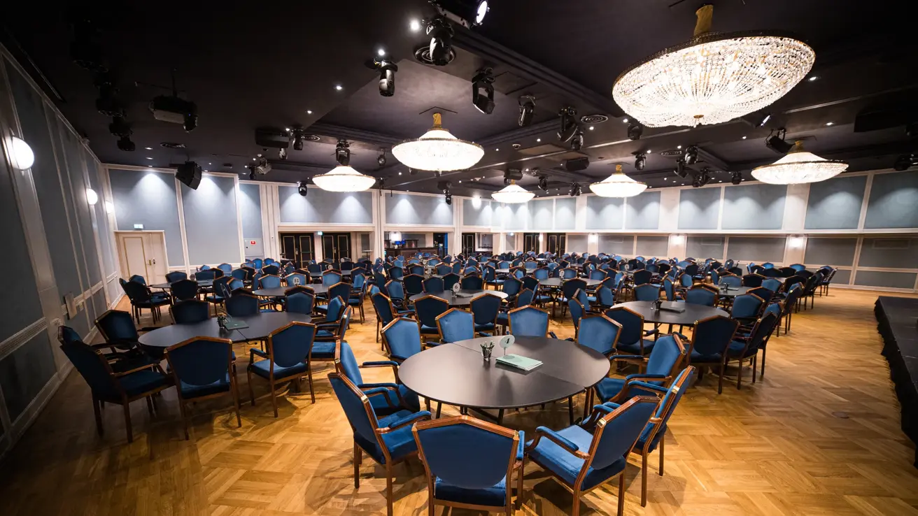 Hall med runde bord, tilhørende blå stoler, parkettgulv og lysekroner i tak
