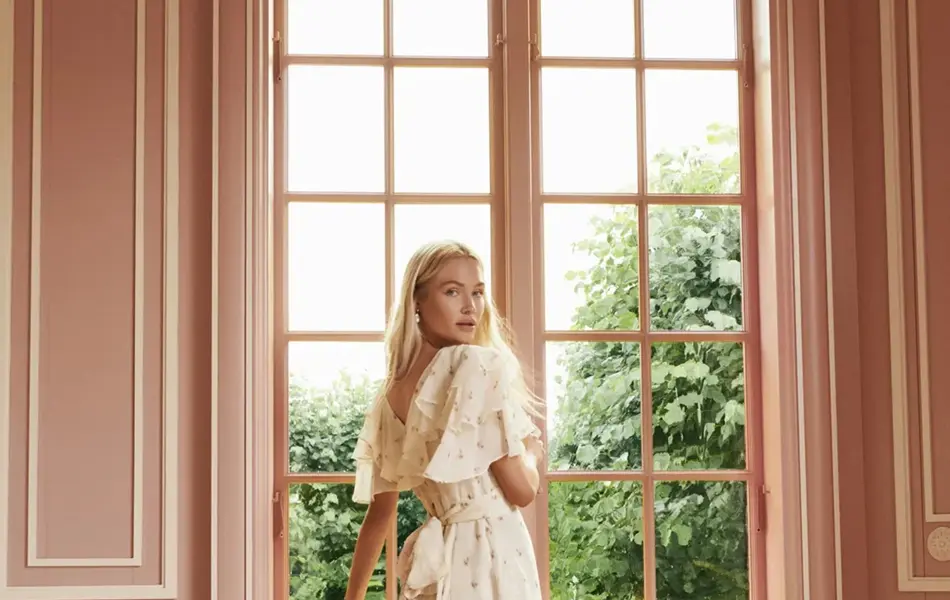 Dame i kjole som står ved et vindu