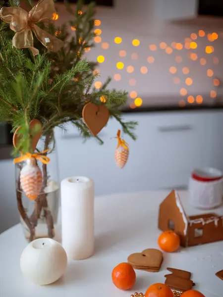 Pepperkakehus og pepperkakehjerter hengende på granbarkvist på julepyntet bord 