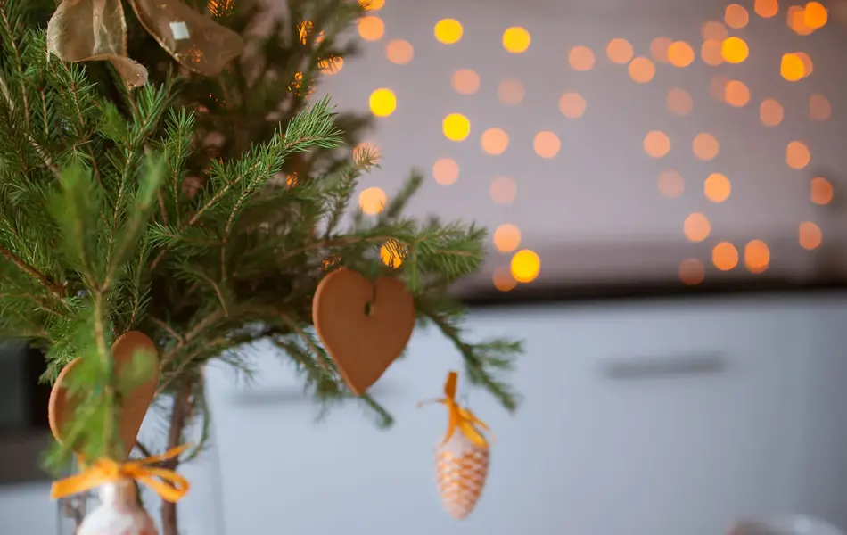 Pepperkakehus og pepperkakehjerter hengende på granbarkvist på julepyntet bord 