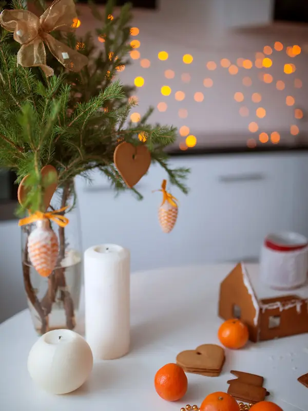 Pepperkakehus og pepperkakehjerter hengende på granbarkvist på julepyntet bord 
