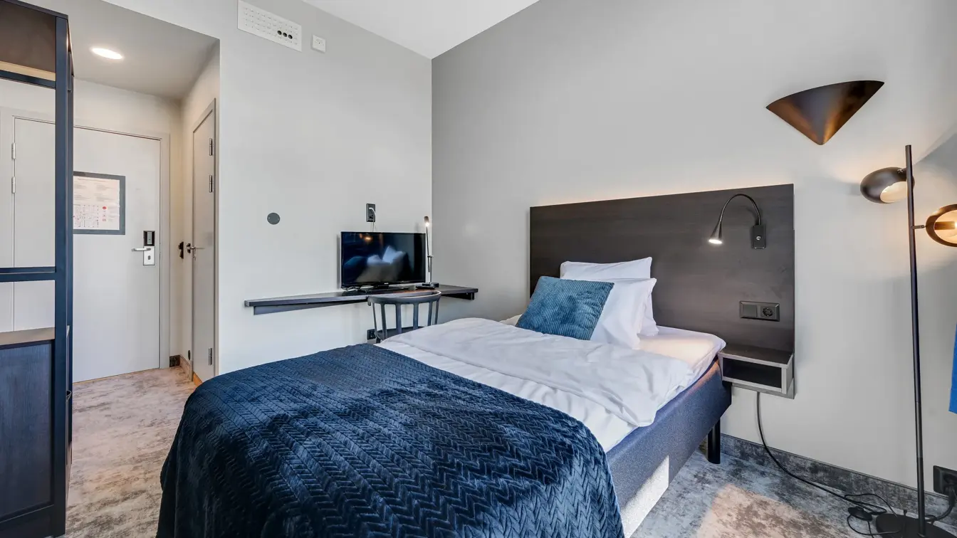 Enkeltseng, hvite vegger, TV, skrivebord, stol. 