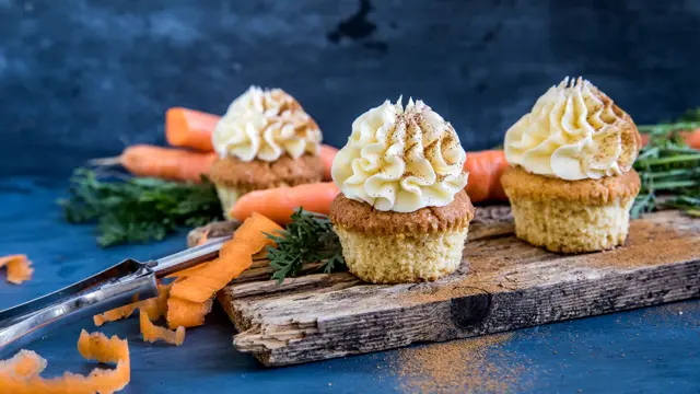 Tre gulerotmuffins med topping på trefjøl omringet av gulerøtter og grønt
