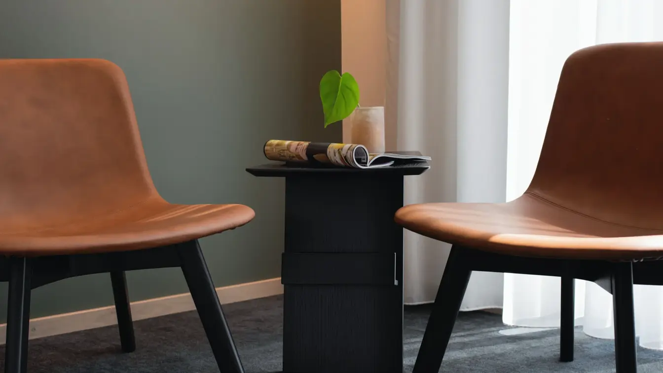 Detaljbilde av to stoler i lysebrunt skinn med sorte ben og lite rundt sort bord mellom.  I standard dobbelt rom på Thon Hotel Norge i Kristiansand.