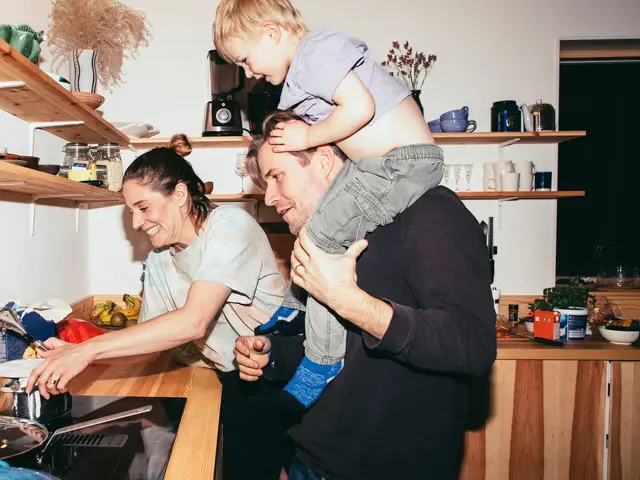 Familie med mor, far og sønn holder på på kjøkken med trebenk og fylte trehyller 