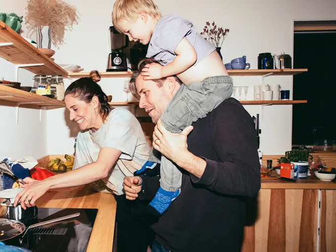 Familie med mor, far og sønn holder på på kjøkken med trebenk og fylte trehyller 