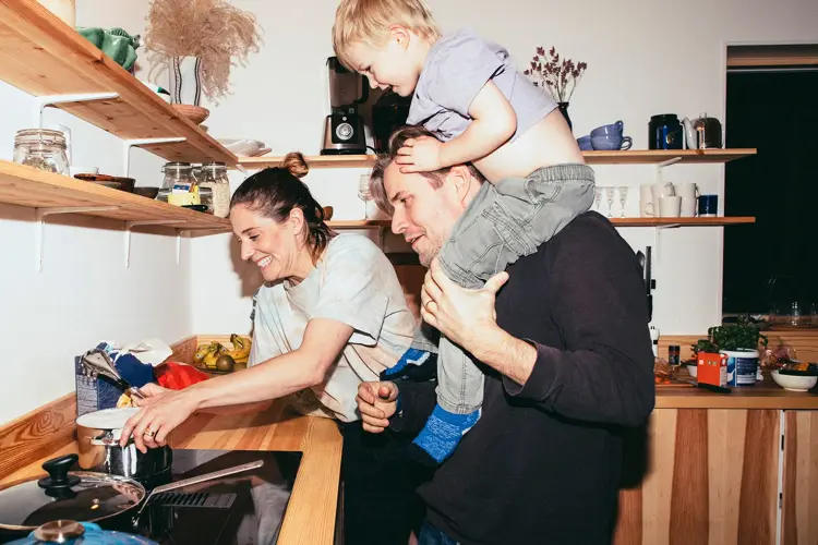 Familie med mor, far og sønn holder på på kjøkken med trebenk og fylte trehyller 