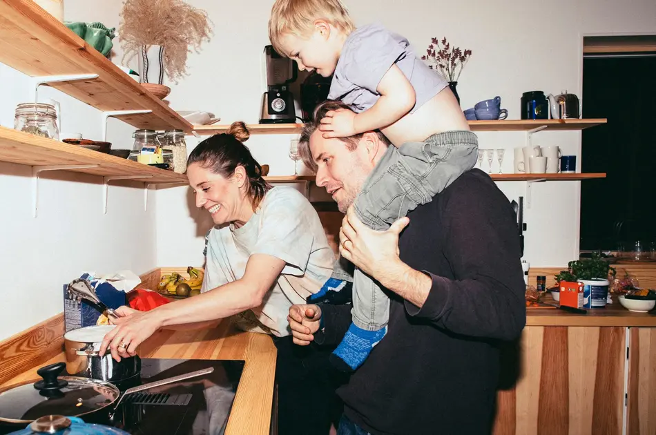 Familie med mor, far og sønn holder på på kjøkken med trebenk og fylte trehyller 