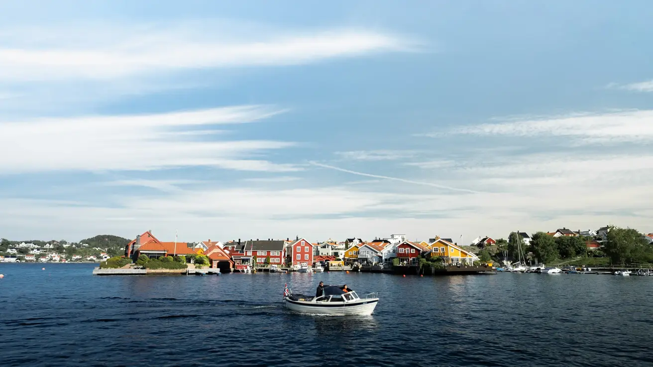 En hvit båt på vannet. I bakgrunnen ses bebyggelse.