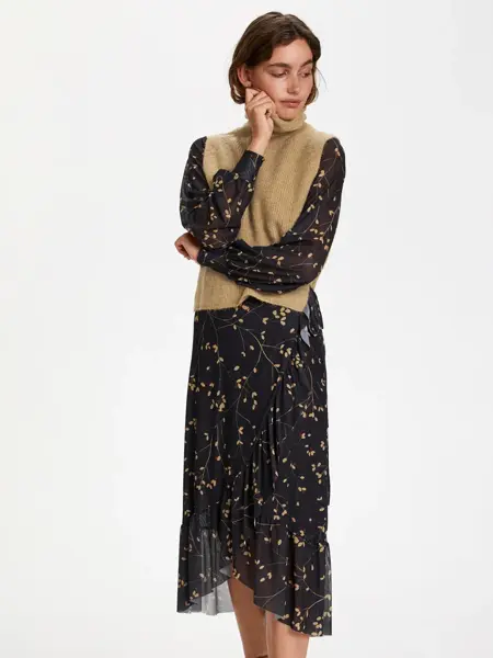 Dame i blomstret kjole og beige vest med høy hals