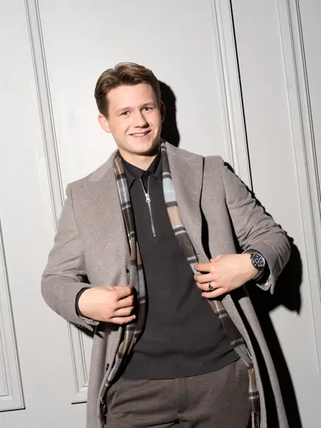 Gutt i beige frakk som smiler mot kamera