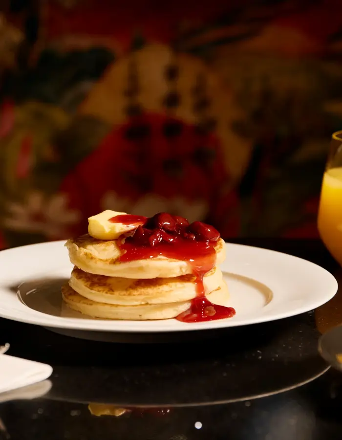 En stabel med pannekaker med smør og syltetøy, kaffekopp og et glass appelsinjuice