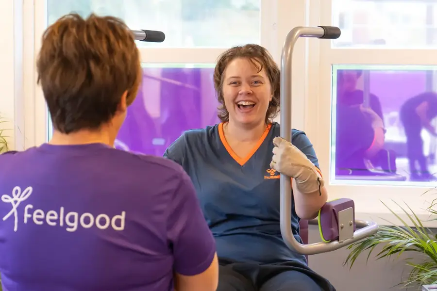 Treningsinstruktør med lille tskjorte med logo "Feelgod" sammen med en som trener på maskin