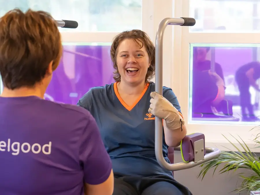 Treningsinstruktør med lille tskjorte med logo "Feelgod" sammen med en som trener på maskin