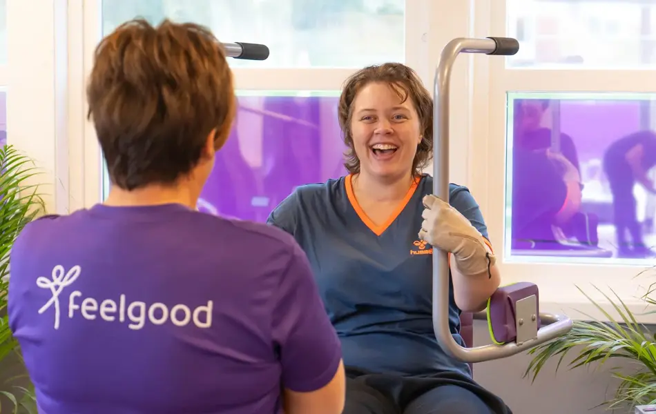 Treningsinstruktør med lille tskjorte med logo "Feelgod" sammen med en som trener på maskin