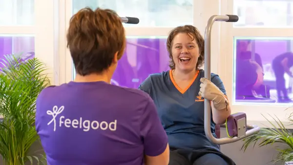 Treningsinstruktør med lille tskjorte med logo "Feelgod" sammen med en som trener på maskin