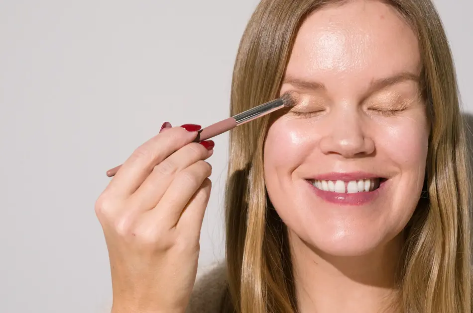 Smilende dame med lukkede øyne tar på seg øyneskygge