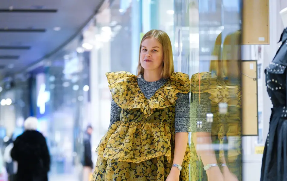 Jente som står og lener seg til en vegg med gul kjole og grå genser under