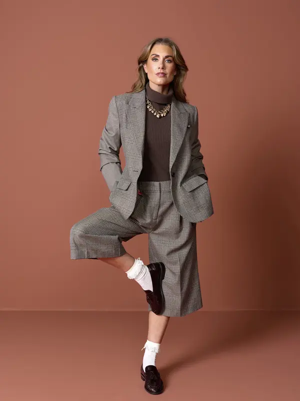 Tone. i brun dressjakke og matchende short, brun genser, hvite sokker og sorte chunky herresko.