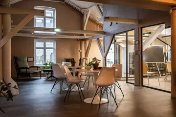 Interiør av sosial sone i Tullins gate 4C med stoler og bord i hvitt, samt synlige kontorrekker langs vinduene med store vinduer