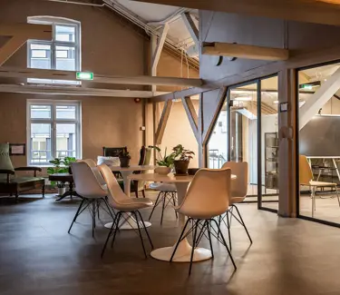 Interiør av sosial sone i Tullins gate 4C med stoler og bord i hvitt, samt synlige kontorrekker langs vinduene med store vinduer