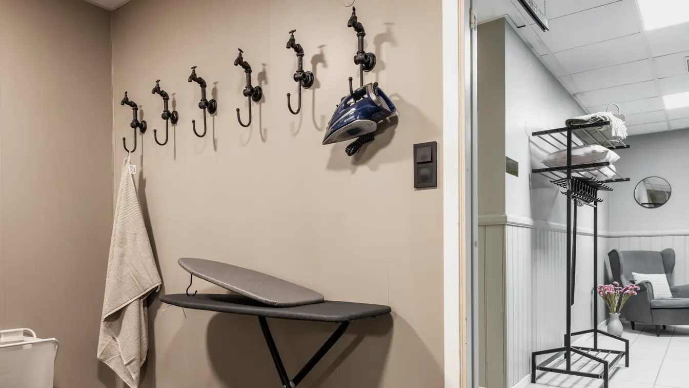 Strykerom med strykebrett, strykejern, store sorte knagger på veggen