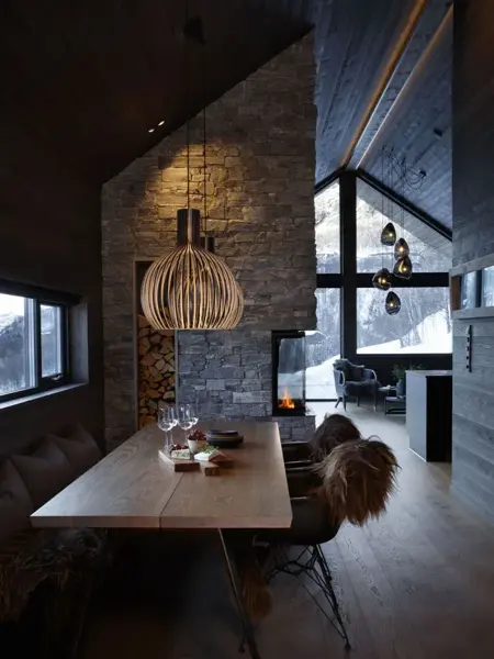 Inne i en fjellhytte med langt spisebord og taklampe over.