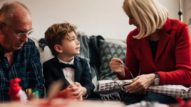 Ung gutt sitter i finstasen mellom sine besteforeldre, hvor bestemor pakker opp julegave